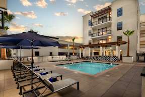 A pool area with sun loungers and a building in the background.