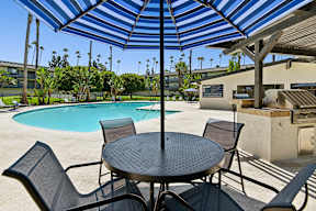 Shaded dining table inside pool area at Oro Apartments next to shaded trellis with bbq grilling stations for poolside picnics