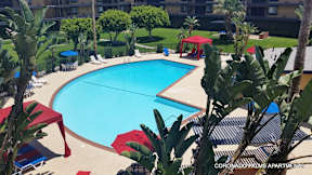 A pool surrounded by red umbrellas and trees.