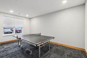 A ping pong table is in the middle of a room with a car and a truck in the window.