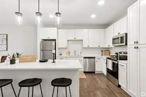 A kitchen with white cabinets and black stools located at Deforest Yards apartments in DeForest, WI