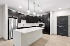 A modern kitchen with a white island and black cabinets located at Deforest Yards apartments in DeForest, WI