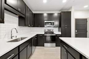 A modern kitchen with black cabinets and stainless steel appliances located at Deforest Yards apartments in DeForest, WI