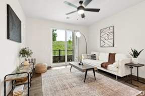A living room with a white couch, a coffee table, and a ceiling fan with a patio located at Deforest Yards apartments in DeForest, WI