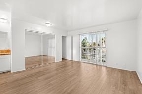 A large empty room with wooden floors and a view of a cityscape through a window.