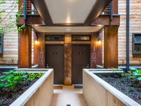 A modern house entrance with a wooden door and a concrete planter on either side.