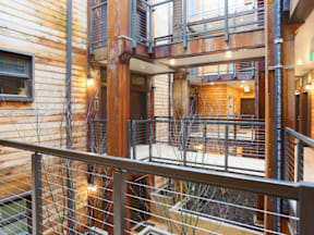 A balcony with a metal railing overlooks a courtyard with a tree and a building in the background.