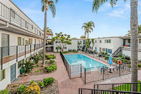 A pool surrounded by a fence and a building in the background.