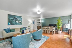 A living room with a blue chair and a painting on the wall.