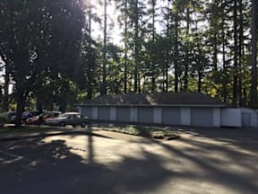 A parking lot with a white building and trees in the background.