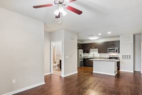 A spacious kitchen and living room with hardwood floors and a ceiling fan.