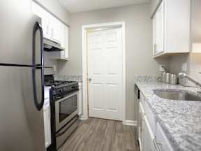 A kitchen with a black refrigerator, stove, and white cabinets.
