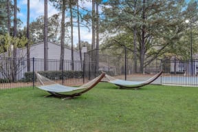 two hammocks in the grass in front of a fence