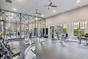 A spacious gym with a variety of equipment and a fan on the ceiling.