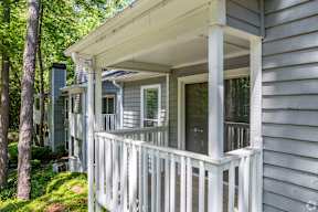 A porch with a white railing and a grey house.