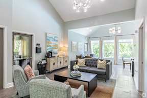 A living room with a grey couch and a grey chair with a red pillow.