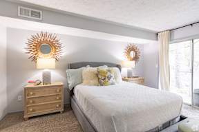 A bedroom with a large bed, a nightstand with a lamp, and two sunburst mirrors on the wall.