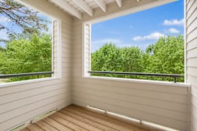 A sunny day with a view of green trees from a wooden balcony.