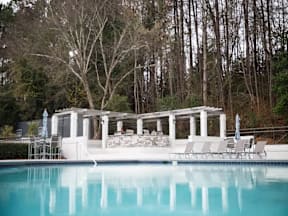 A pool with a white pergola and chairs around it.