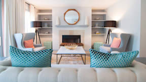 A living room with a fireplace and two chairs with patterned cushions.