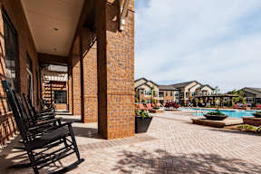A patio with chairs and a pool in the background.
