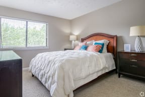 A bedroom with a large bed and a window with blinds.