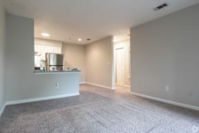 A spacious living room with a carpeted floor and a kitchenette in the corner.