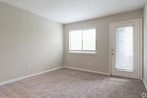 A room with a carpeted floor, a window with blinds, and a door.