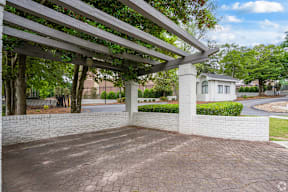 A white house is seen under a wooden pergola.