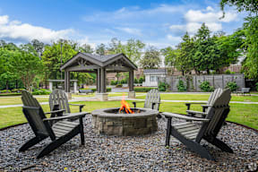 A fire pit is surrounded by three Adirondack chairs in a backyard.