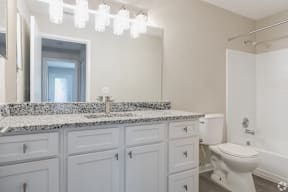 A white bathroom with a marble counter top and a white toilet.
