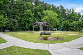 A gazebo sits in the middle of a park with a paved walkway.