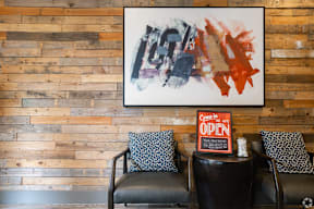 A painting hangs on a wooden wall above a black leather couch with a sign that says "Come in, open.".