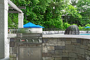A BBQ grill is on a stone patio next to a pool.
