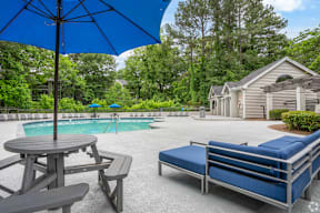 A blue umbrella is over a picnic table next to a pool.