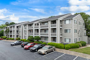 A parking lot in front of a grey apartment building with cars parked.