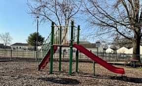 A red slide on a playground with a green metal frame.
