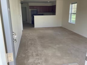 an empty living room with a kitchen in the background