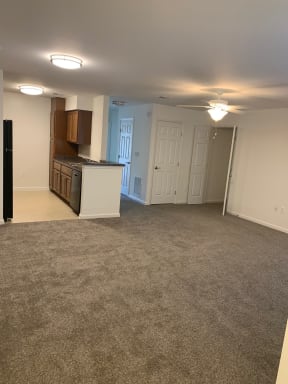 an empty living room with a kitchen in the background
