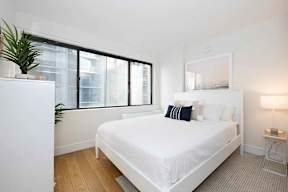 A white bed with a white mattress and pillows in a room with a window.