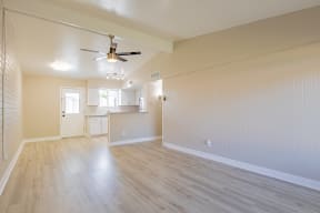 an empty living room with a ceiling fan and a kitchen in the background