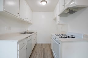 an empty kitchen with white cabinets and a stove and sink