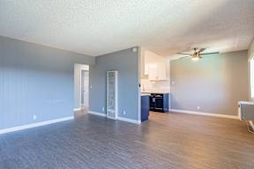 A spacious room with a ceiling fan and a kitchenette.
