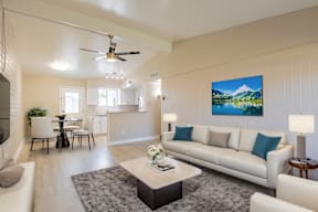 A living room with a white couch and a painting of a mountain scene on the wall.