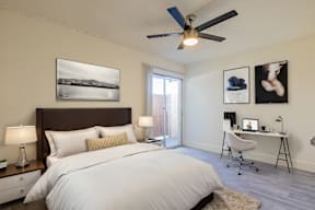 A bedroom with a large bed, a desk with a chair, and a ceiling fan.