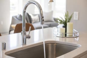 a kitchen sink with a faucet and a living room in the background