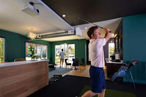 A man is playing golf in a room with a green wall.