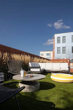 A patio with a table, chairs, and a couch with a building in the background.