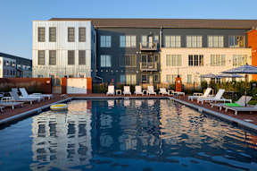 A large swimming pool in front of a building with lounge chairs around it.