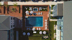 A pool surrounded by a patio with chairs and umbrellas.